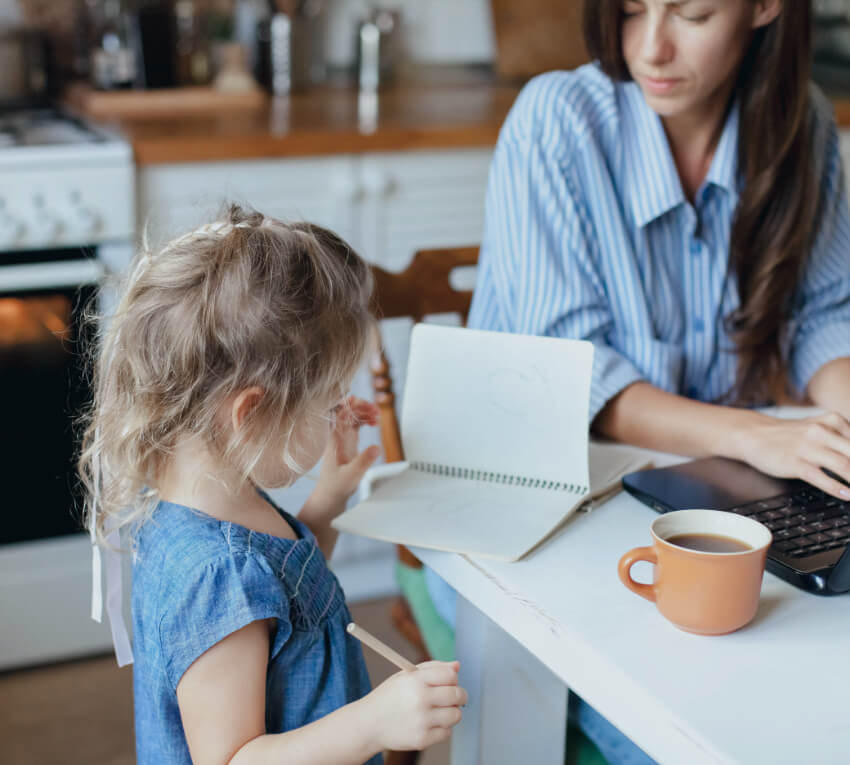 Woman and child in kitchen. Woman typing on her laptop and child writing in notebook